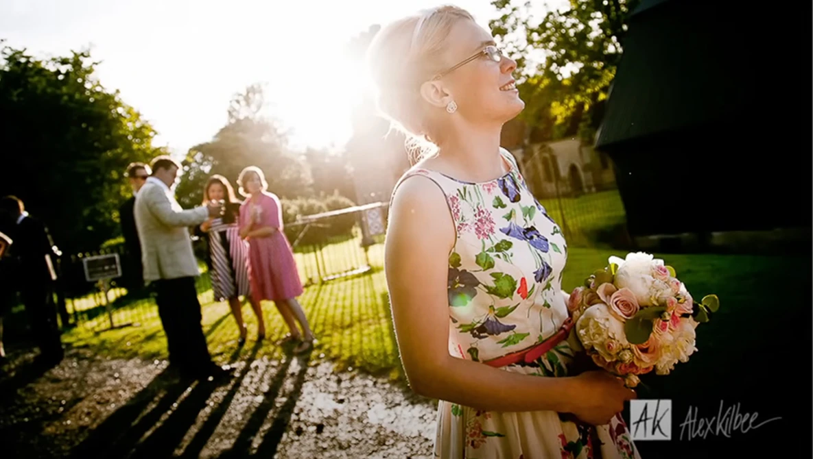 Bride in floral dress holding peach bouquet at outdoor garden wedding ceremony during golden hour.