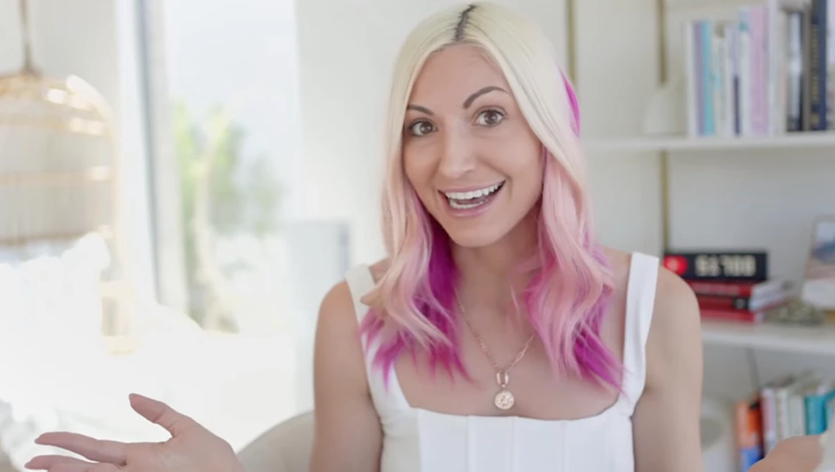 Woman with blonde and pink ombre hair smiling at camera in bright interior space.