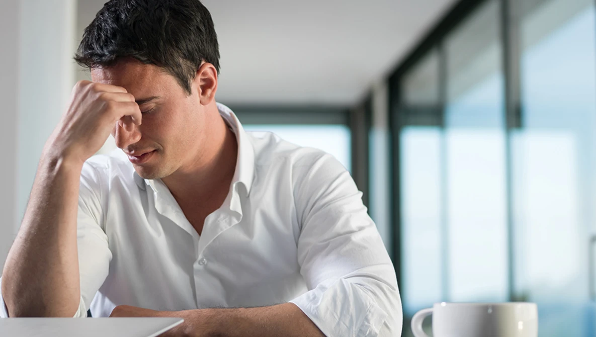 Man in white shirt with hand to face, appearing stressed or contemplative at desk.
