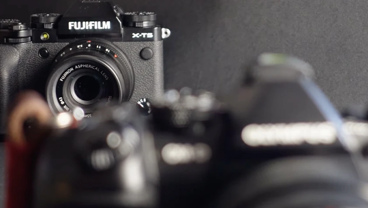Fujifilm X-T5 mirrorless camera in sharp focus with additional camera gear blurred in the background.