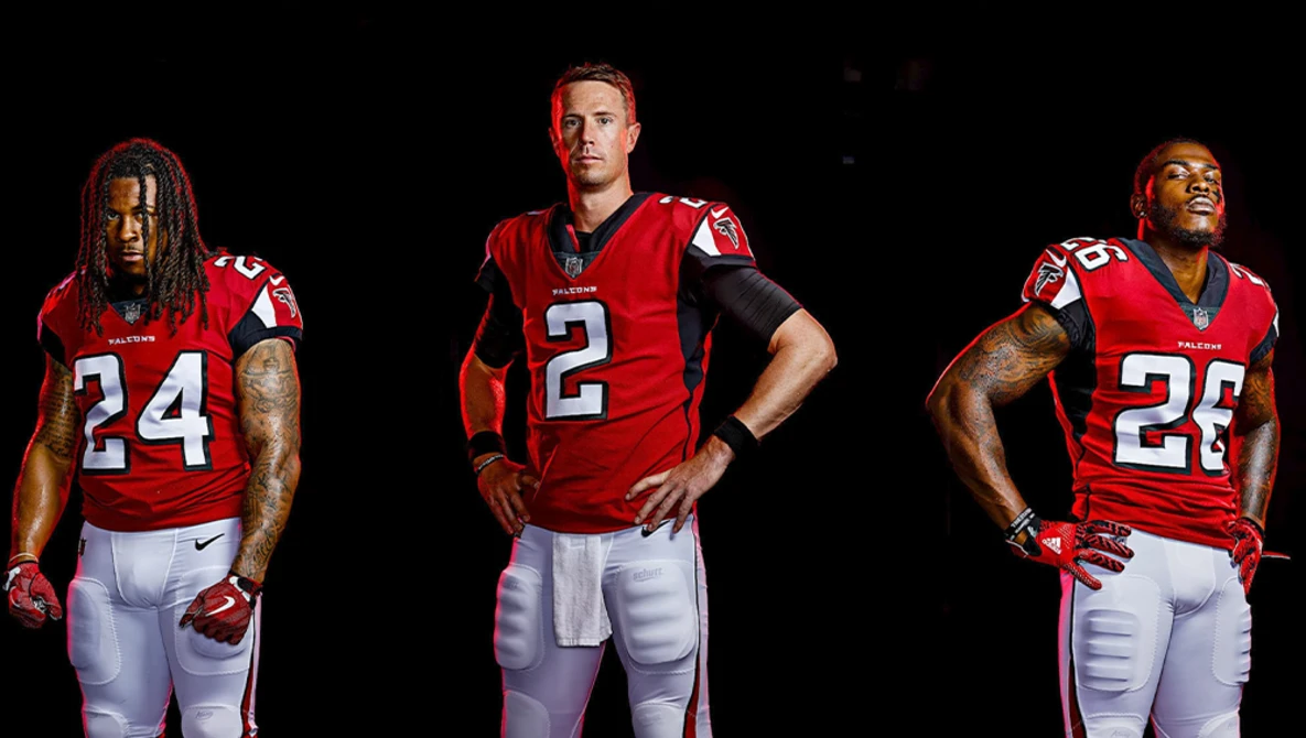 Three football players in red jerseys posed against black background.