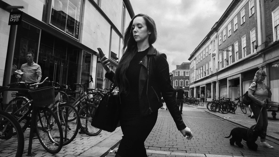 Woman in dark jacket walking down a European cobblestone street lined with bicycles and period buildings.