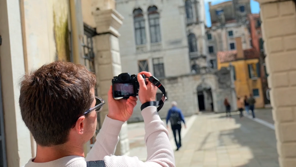 Photographer holding a camera at arm's length to frame a historic European plaza with classical architecture.