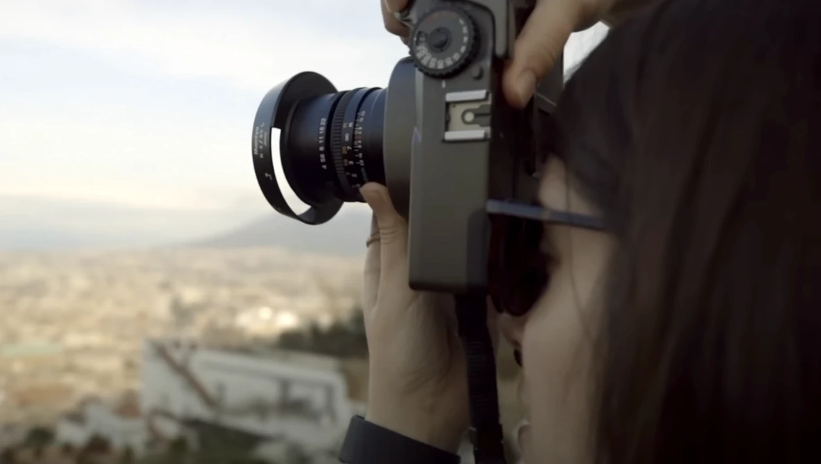 Photographer holding a vintage film camera with telephoto lens, capturing an aerial cityscape view.