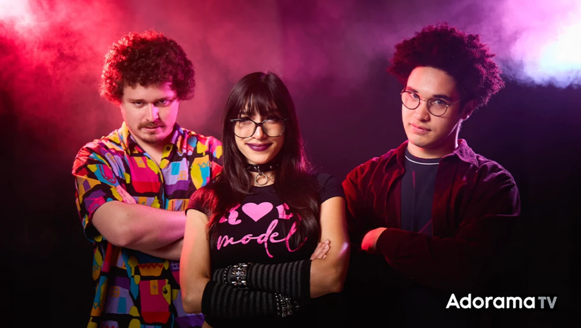 Three people posing against a pink and purple gradient backdrop with dramatic colored lighting.