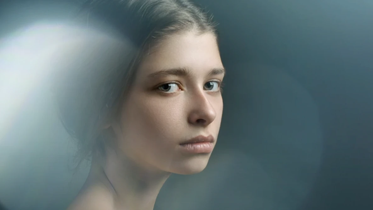 Young woman in profile against a dark teal background with soft directional lighting.
