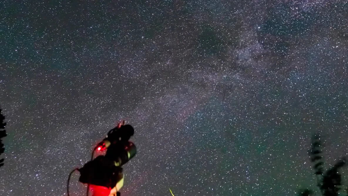 Telescope pointed at night sky filled with stars and Milky Way with red light attachment.