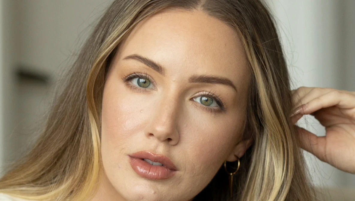 Woman with long brown hair and green eyes looking directly at camera with neutral expression.