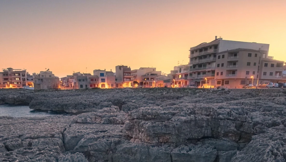Coastal buildings lit by golden hour sunlight against rocky shoreline at dusk.