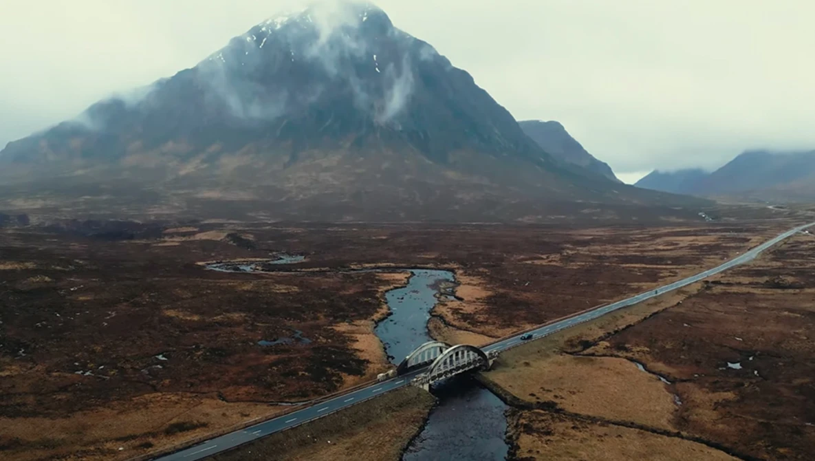 Aerial view of a mountain with a road and river crossing a barren landscape.