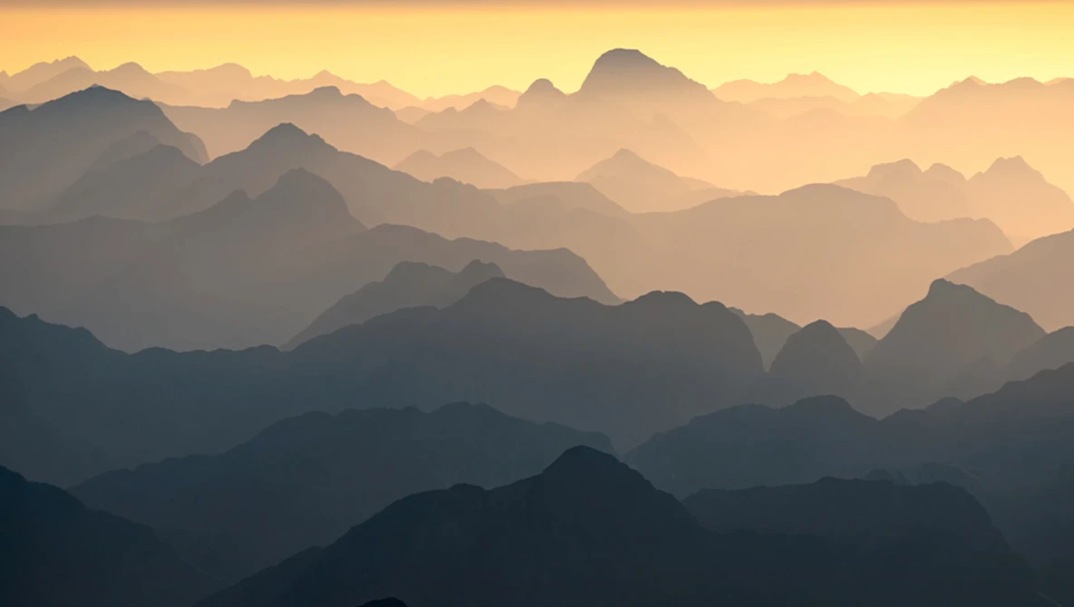 Layered mountain silhouettes fading into atmospheric haze at sunrise or sunset.