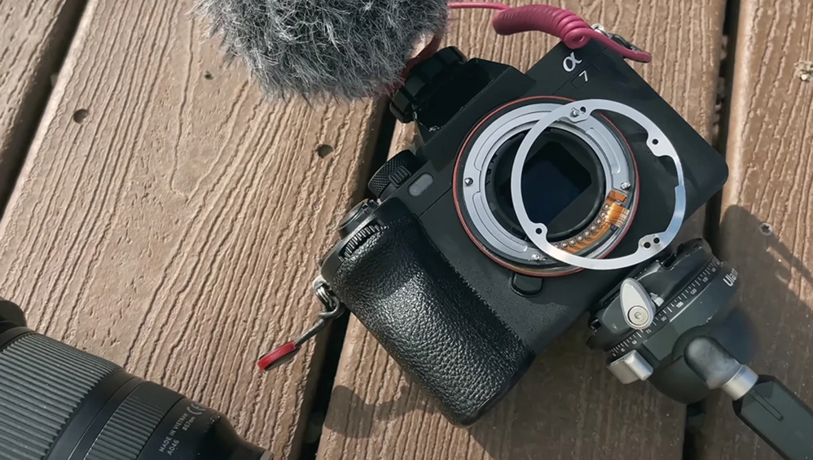 Mirrorless camera with lens removed, showing mount adapter and internal mechanics on wooden surface.