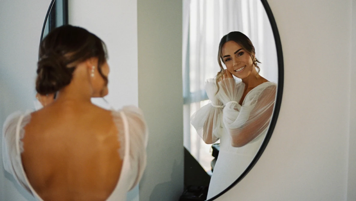 Woman in white shirt viewed from behind looking at her reflection in a round mirror.