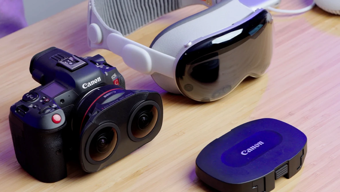 Canon RF mirrorless cinema camera with dual lenses displayed on wooden surface alongside accessories.