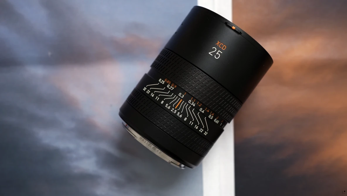 Black telephoto lens with focal length markings displayed against a dramatic cloudy sky backdrop.