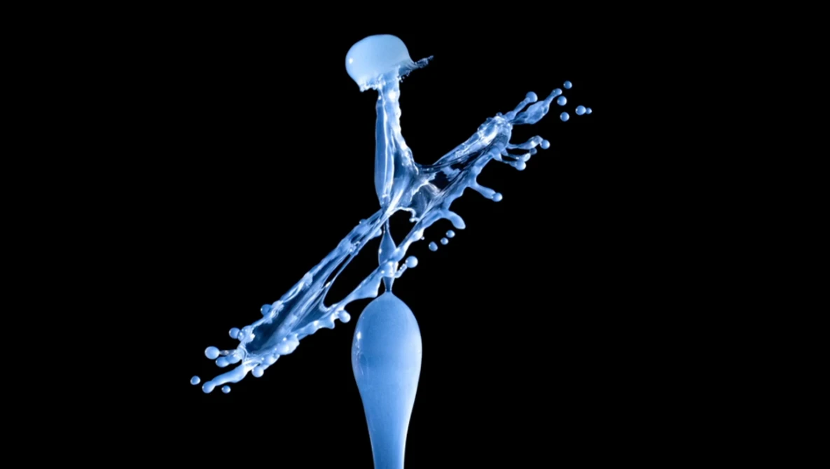 Blue water splash captured mid-air against a black background, with droplets suspended in dynamic motion.