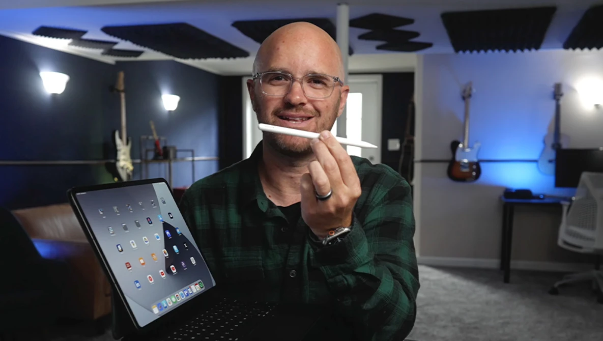 Man in a recording studio holding a tablet and stylus while smiling at the camera.