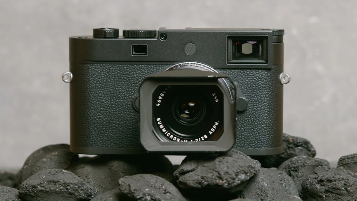 Leica M rangefinder camera with gray textured body and chrome lens, positioned on rough gray stones.