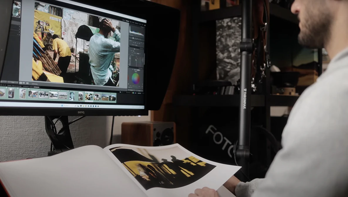 Photographer reviewing edited images on monitor while holding color-corrected print.