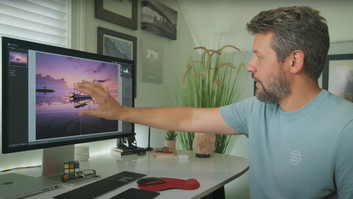 Photographer pointing at sunset landscape image on monitor during editing session.