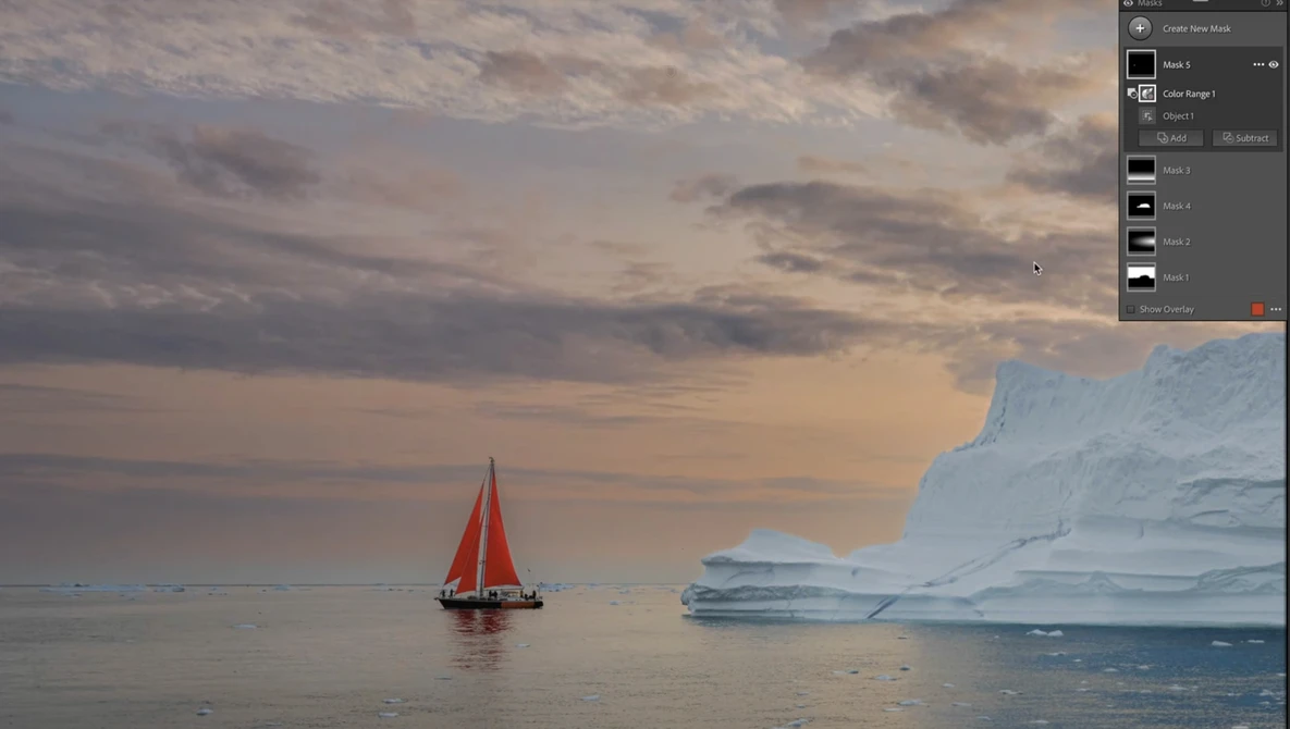 Red-sailed boat on calm water with large icebergs under a dramatic cloudy sky.