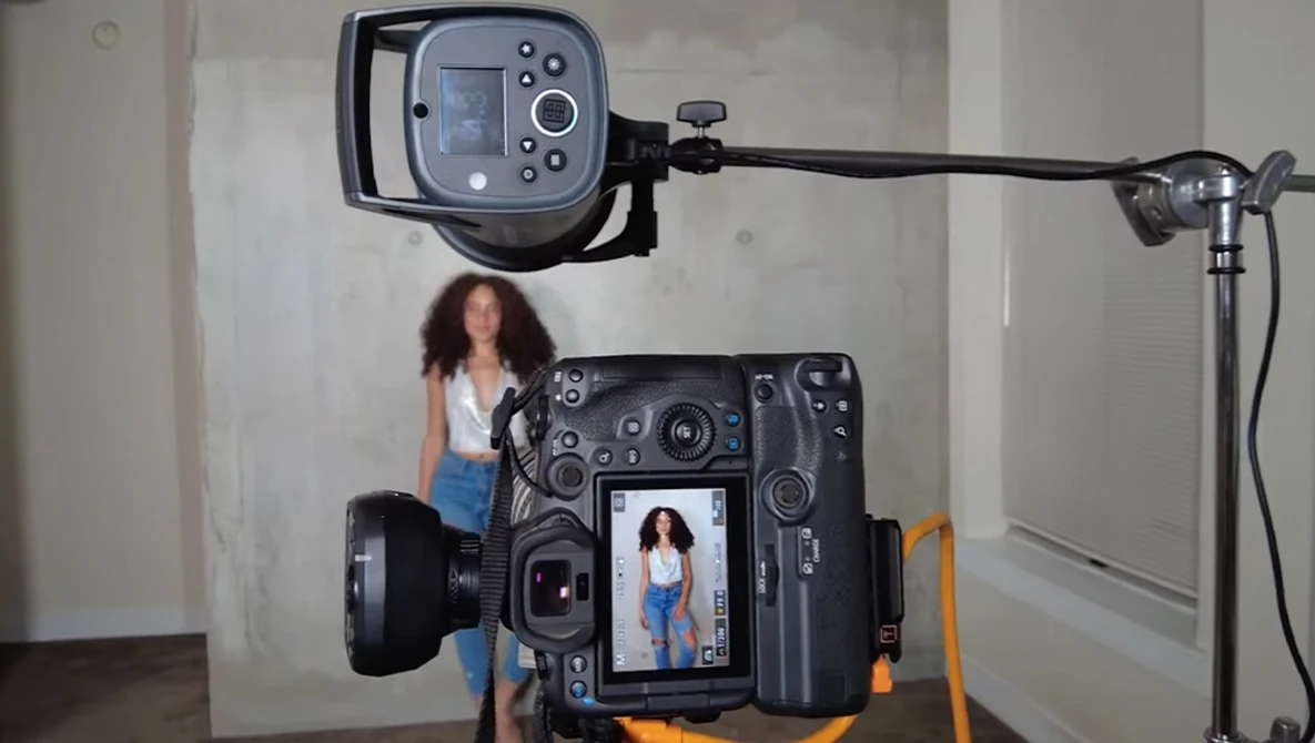 Behind-the-scenes view of a portrait photography setup with a large-format camera displaying a live image of a woman on its LCD screen.