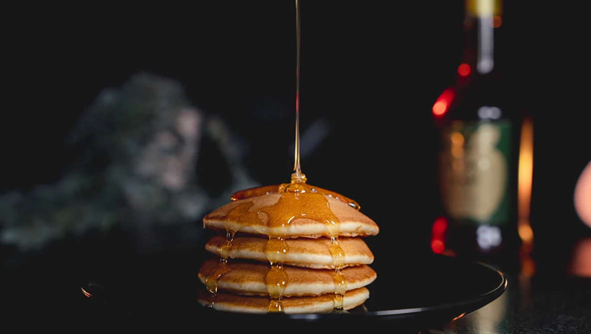 Stack of golden pancakes with syrup being drizzled over the top.