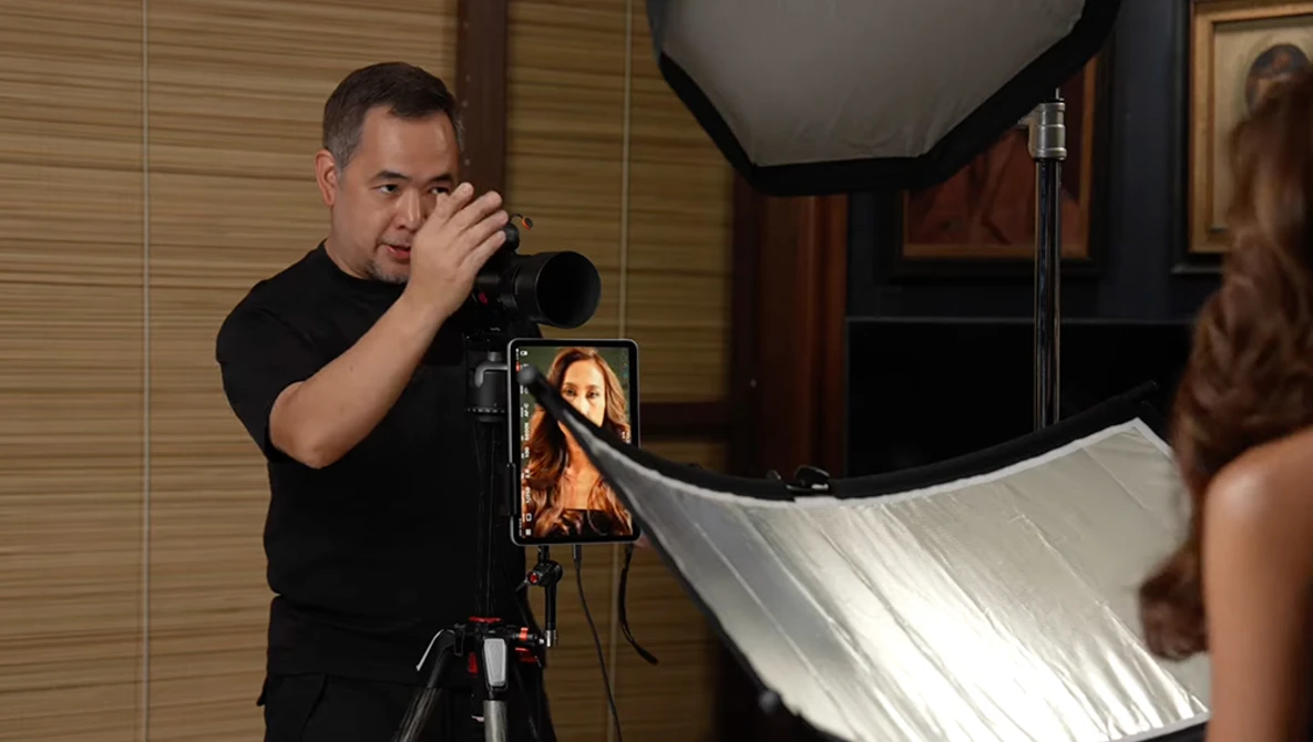 Photographer with camera on tripod positioning a reflector during a portrait lighting setup.