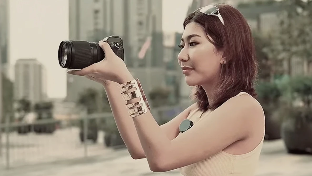 Female photographer holding DSLR camera up to her eye while composing a shot of an urban skyline.