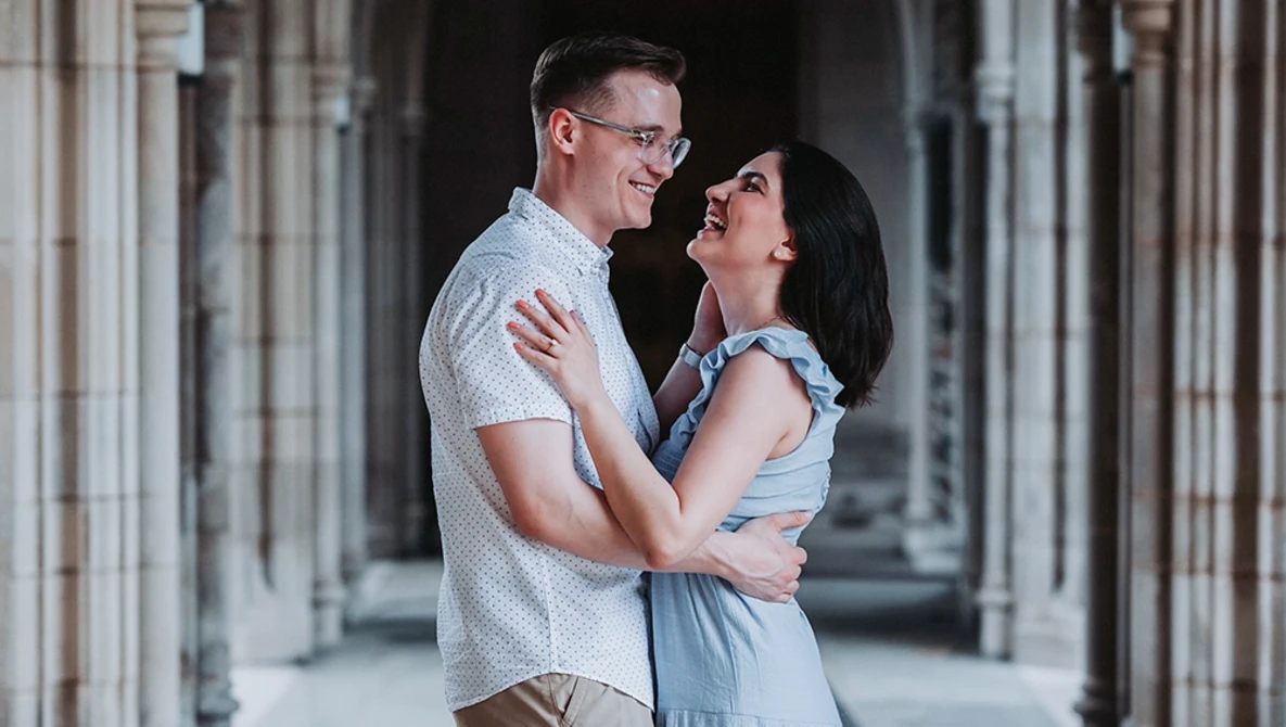 Couple smiling at each other in a columned hallway with soft natural light.
