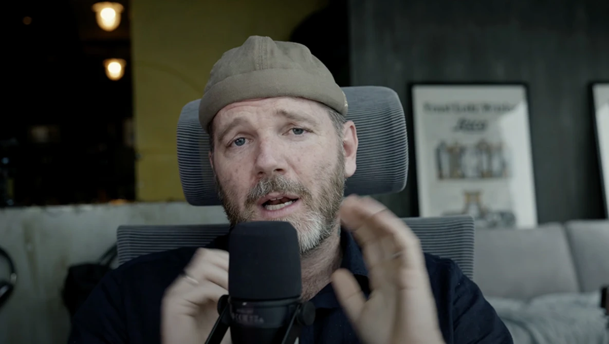 Man speaking into a microphone while wearing a beanie cap in a studio setting.
