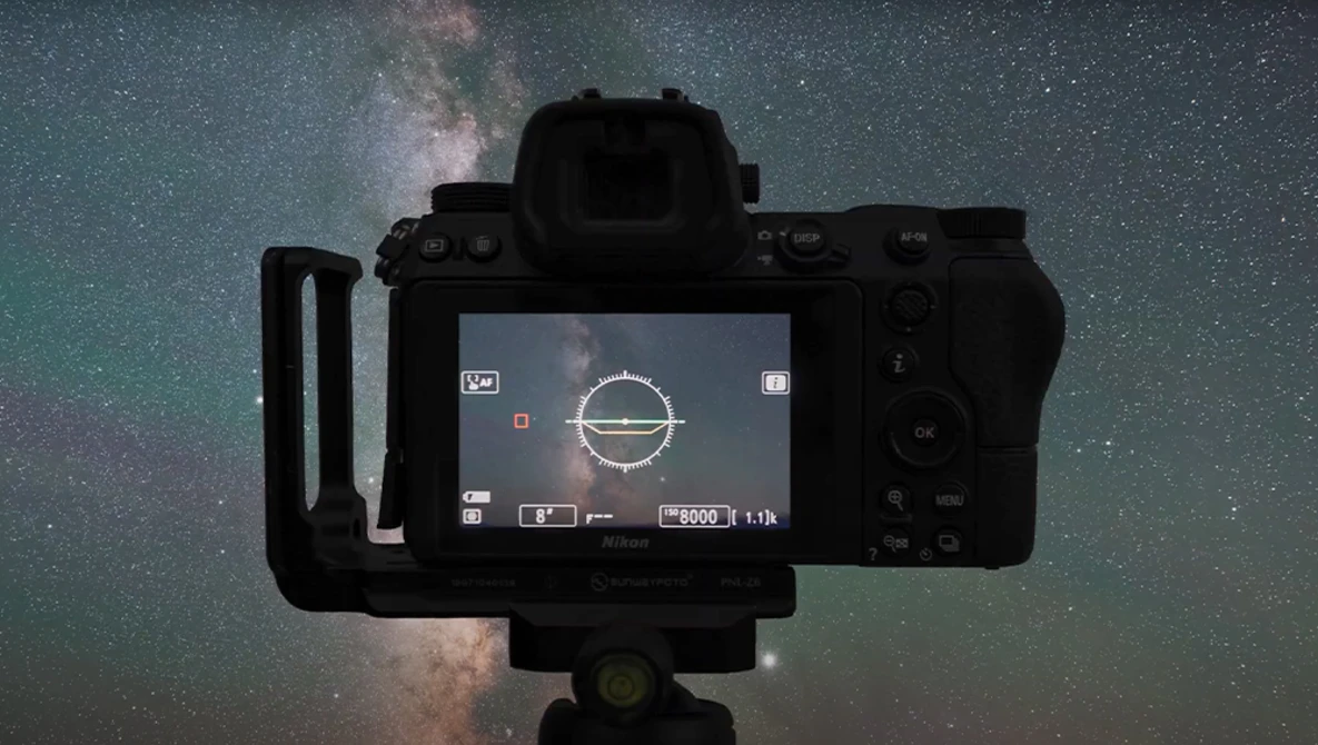 Mirrorless camera mounted on tripod displaying live view of Milky Way galaxy against starry night sky.