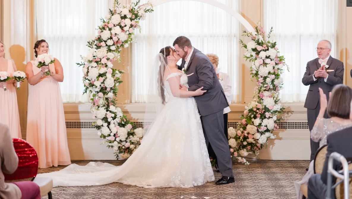 Bride and groom kiss at the altar beneath a floral arch during wedding ceremony.