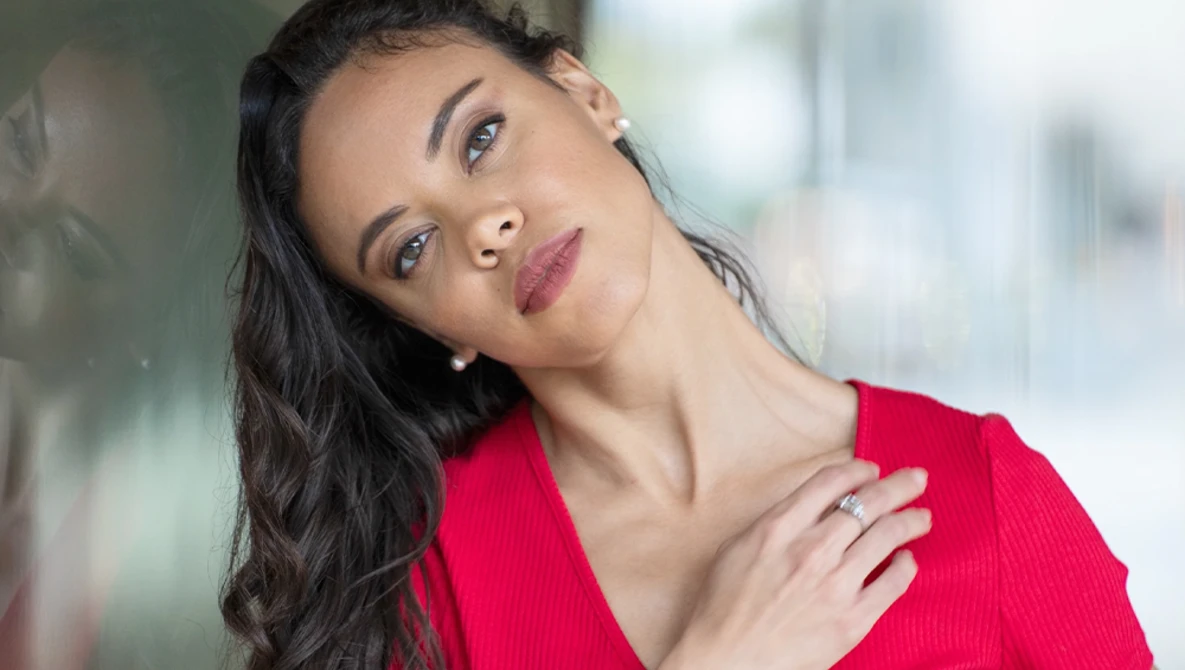 Woman in red top tilting head against blurred urban background.