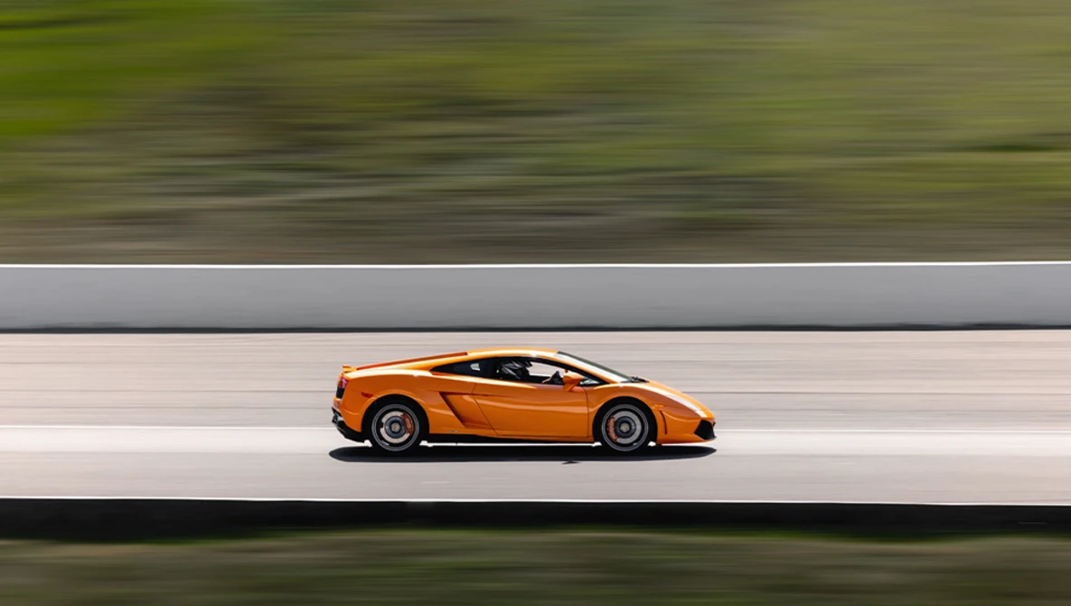 Orange sports car in profile against blurred green and gray background.