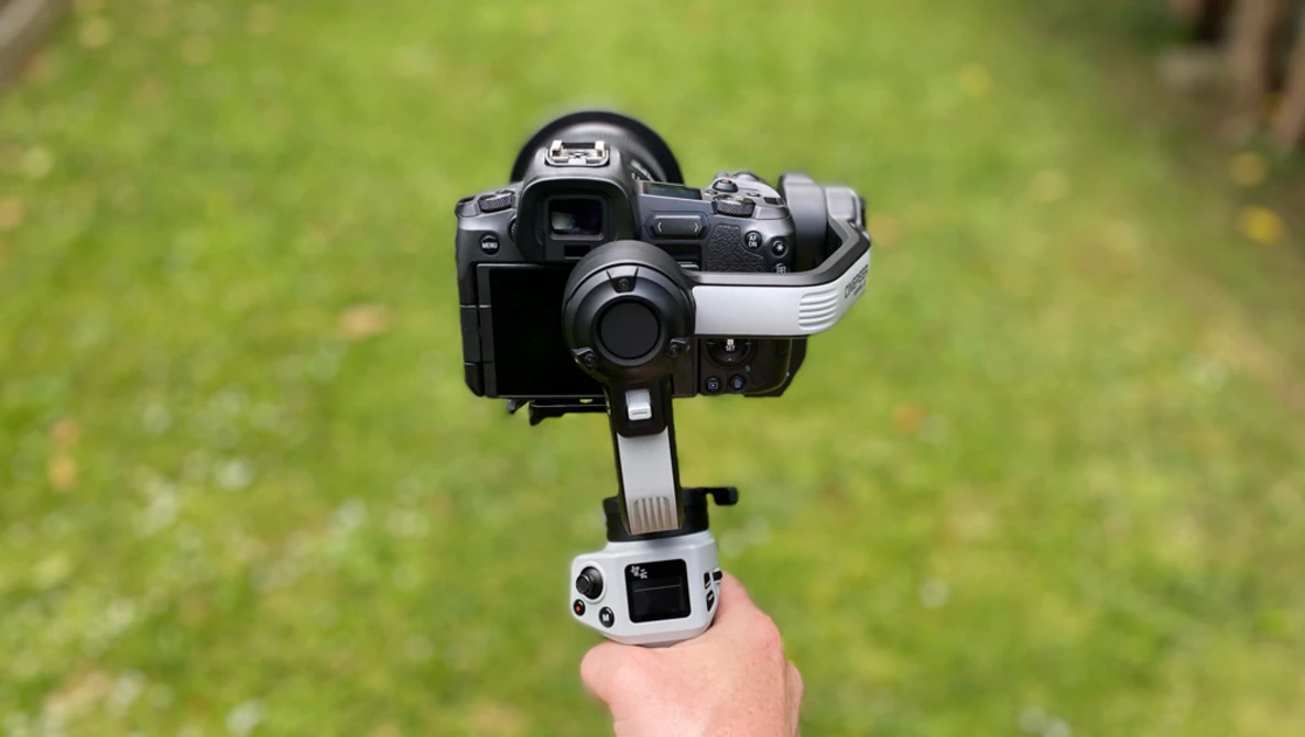 Camera mounted on a motorized gimbal stabilizer held in a person's hand against a blurred green outdoor background.