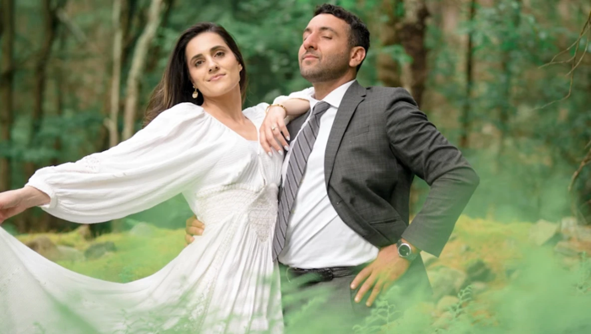 Bride and groom posing together in a forest setting with flowing white fabric.