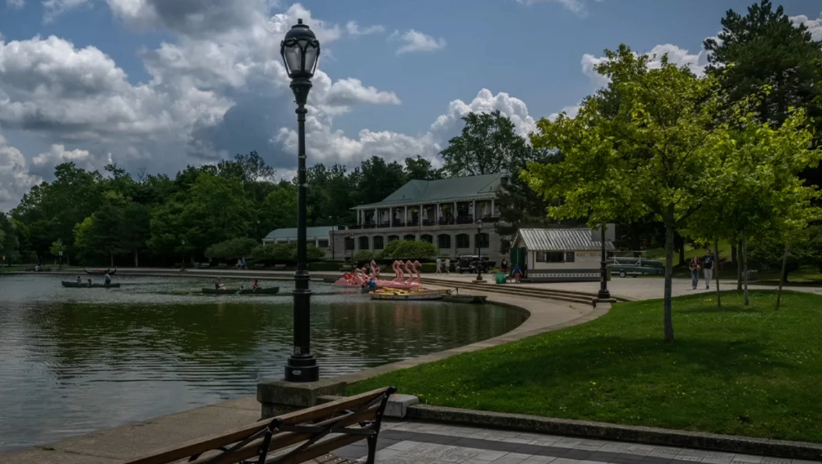 Lamppost on wooden dock overlooking a calm lake with historic building and trees under blue sky.