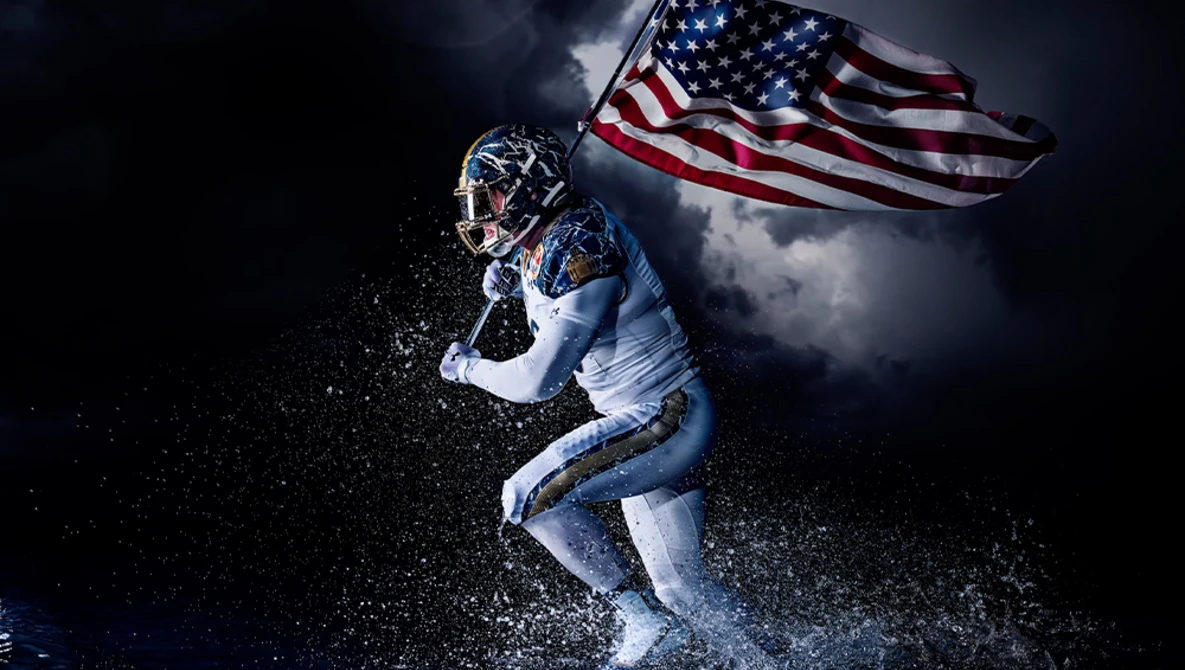 Football player in white uniform catches ball with American flag in dramatic stormy background.