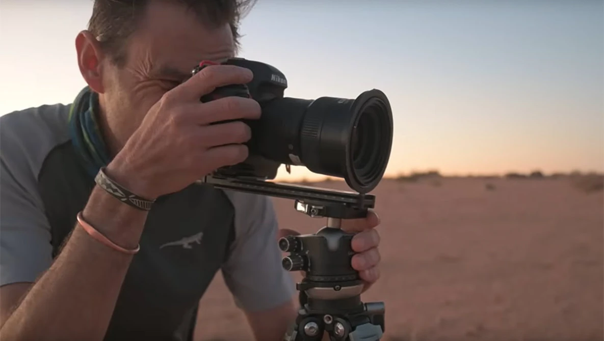 Photographer holding a DSLR camera mounted on a tripod head while composing a shot during golden hour.