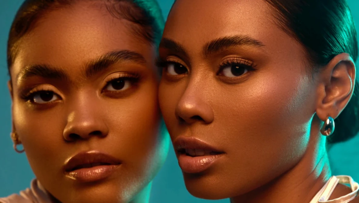 Two women with warm-toned skin positioned close together against a turquoise background.