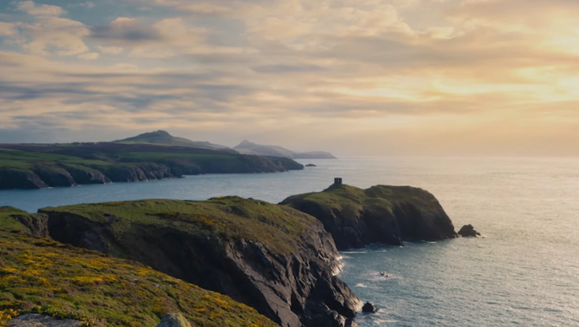 Dramatic coastal cliffs and headlands overlooking calm sea under golden-hour sky.