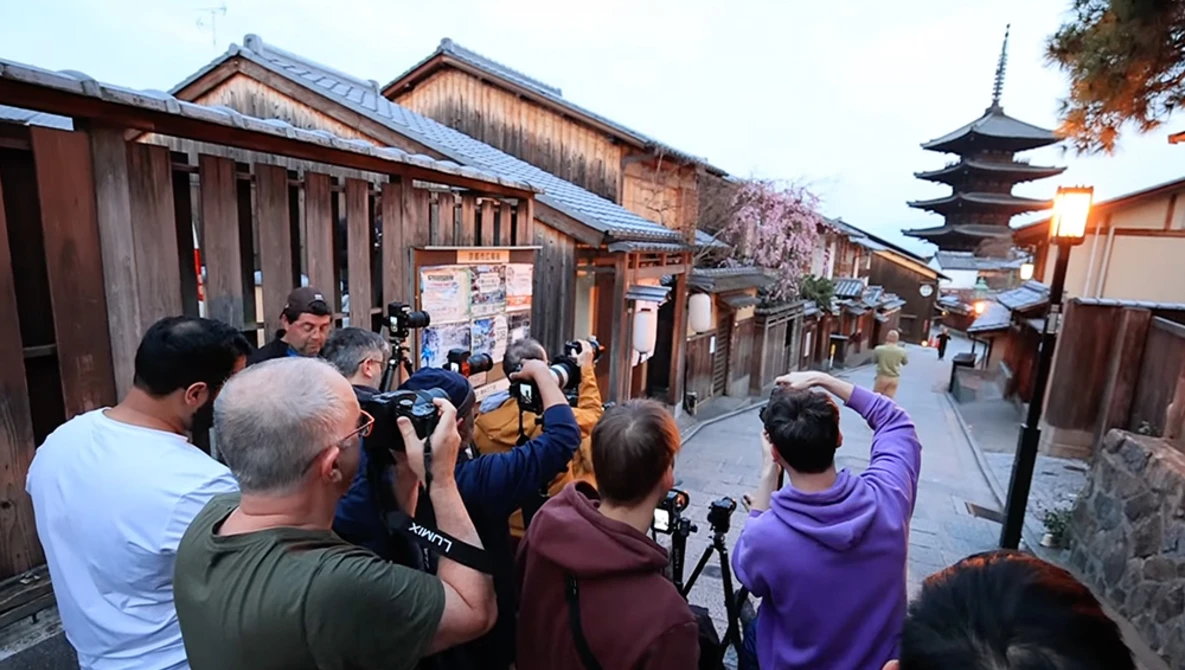Group of photographers with cameras photographing a traditional Japanese street lined with wooden buildings and a pagoda in the background.