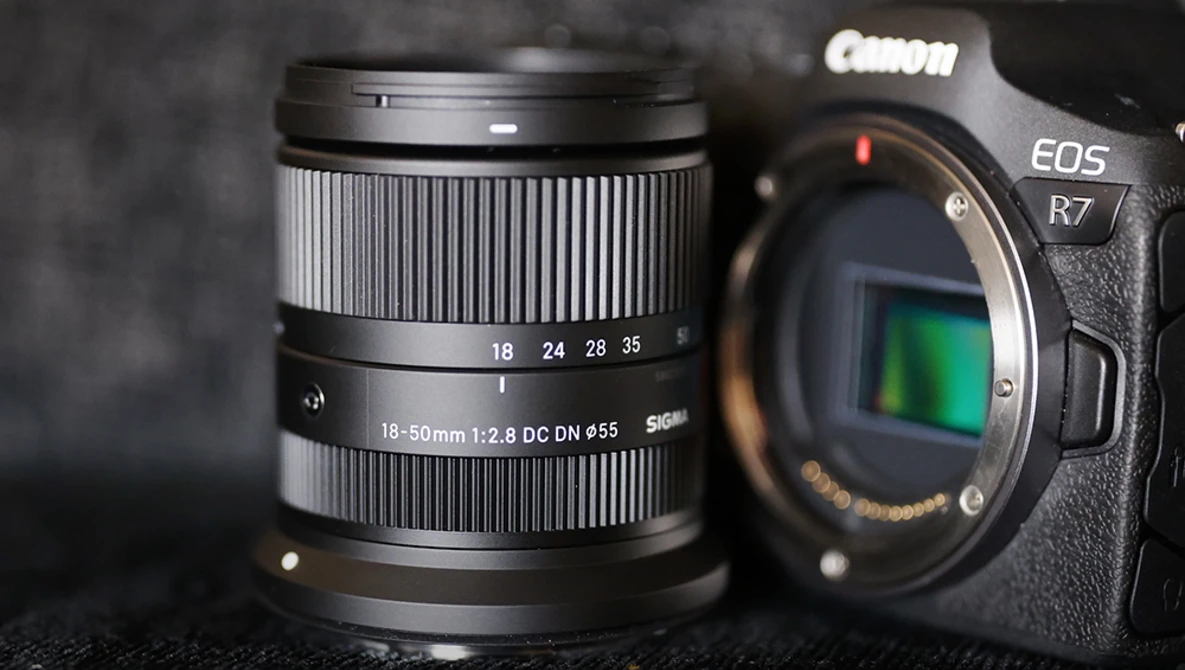 Canon EOS R7 camera body with Canon RF 18-50mm f/2.8 DC DN Contemporary lens on dark surface.