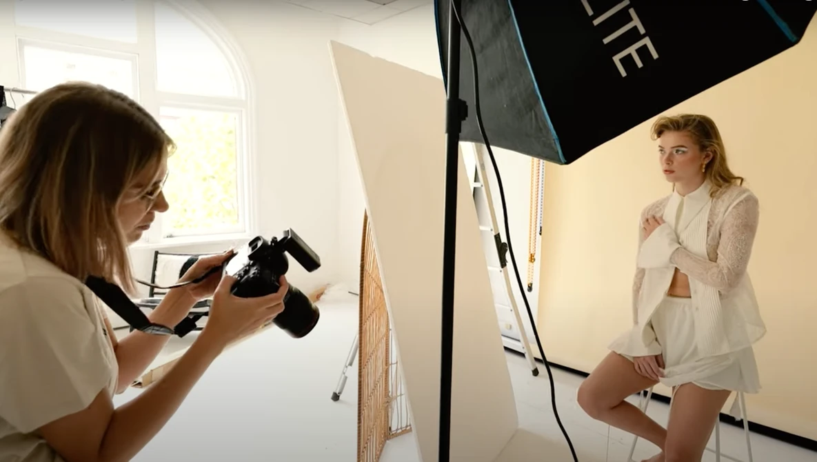 Photographer holding a camera while shooting a model in a studio setting with professional lighting equipment.