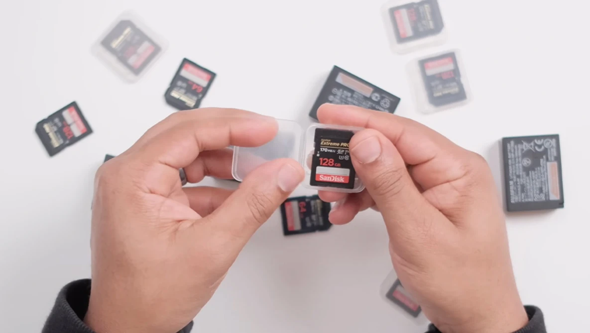 Hands holding SD memory cards with additional cards scattered on white surface.
