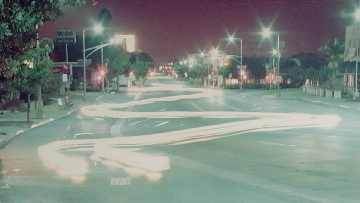 Empty nighttime street intersection with long exposure light trails creating flowing patterns across the pavement.