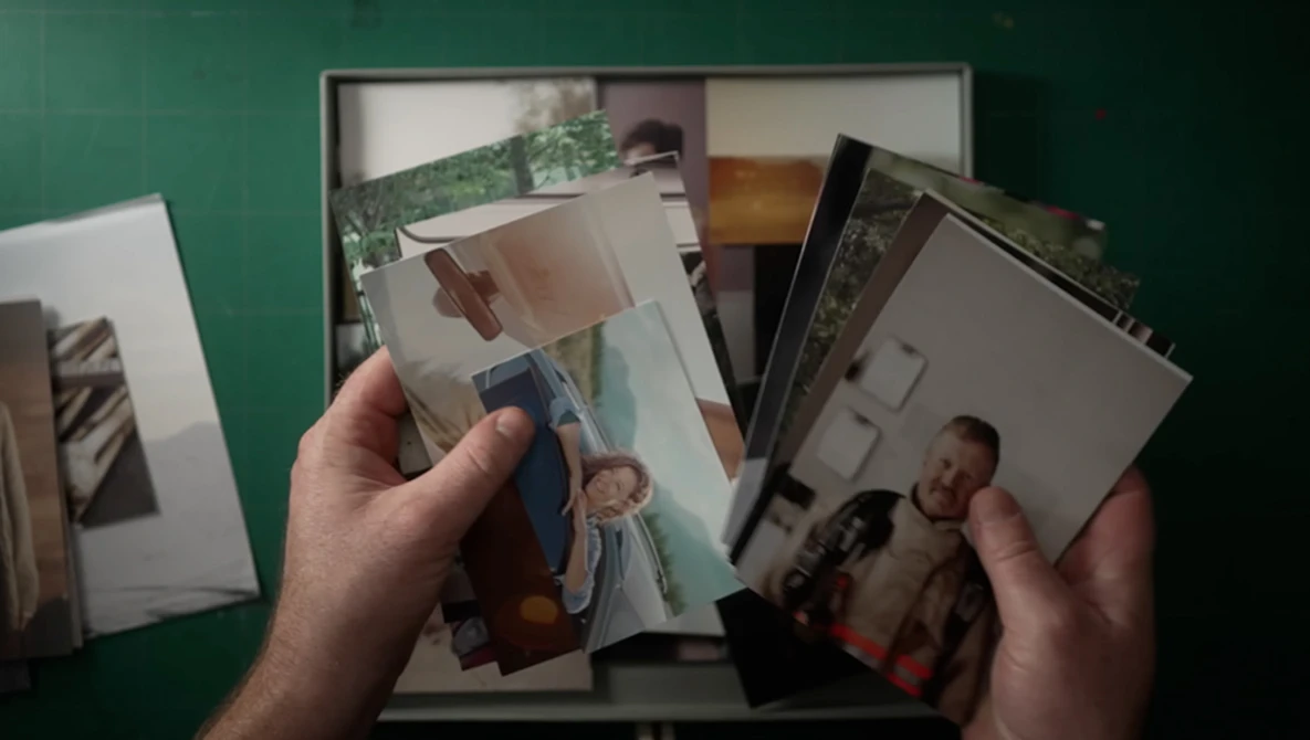 Hands holding scattered printed photographs against a green background with more prints visible below.