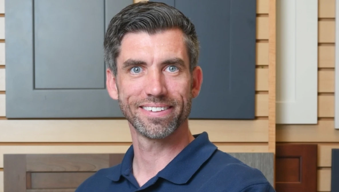 Man with dark hair and beard smiling at camera wearing navy polo shirt.