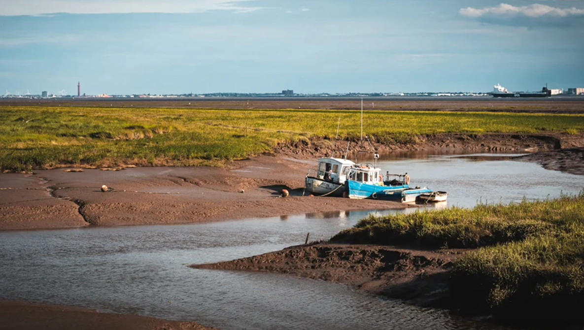 Fishing boat stranded on mudflats beside a shallow tidal channel during low tide.